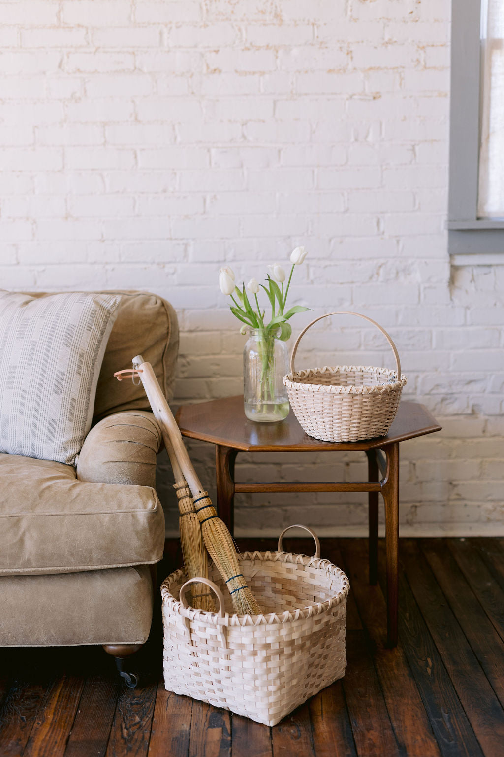 Living room with beige sofa, wicker baskets, and a small wooden table against a white brick wall.
