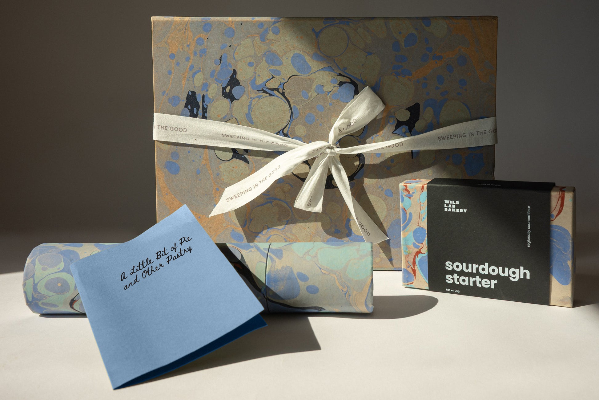 Gift box with a bow, blue card, and black box labeled 'sourdough starter' on a neutral background