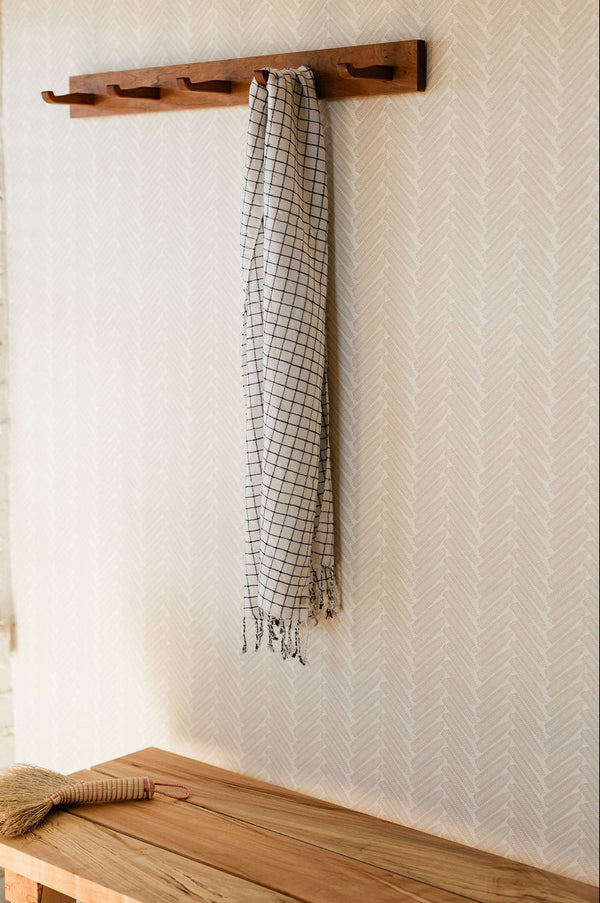 Wooden coat rack with a checkered towel hanging on a wall next to a wooden bench.